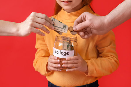 Little girl and parents putting money for her education in jar against color backgroundの写真素材
