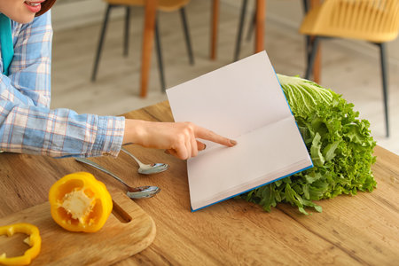 Young woman with recipe book cooking in kitchenの写真素材