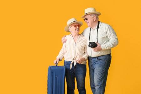 Happy senior couple with packed suitcase on color backgroundの写真素材