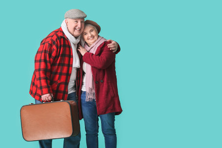 Happy senior couple with packed suitcase on color backgroundの写真素材
