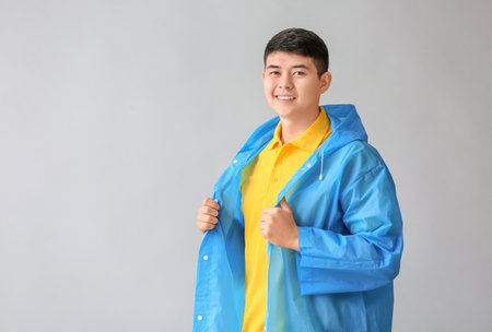 Young Asian man in raincoat on gray backgroundの写真素材