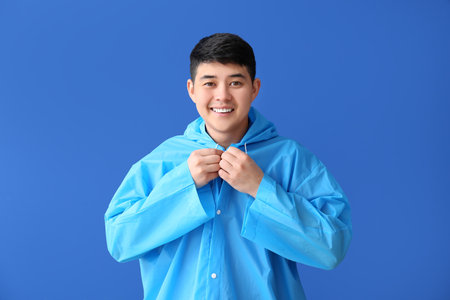 Young Asian man in raincoat on color backgroundの写真素材
