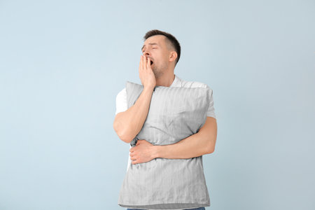Tired man with pillow on color background. Concept of sleep deprivationの写真素材