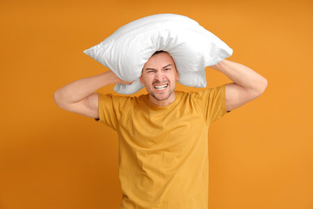 Angry man with pillow on color background. Concept of sleep deprivationの写真素材