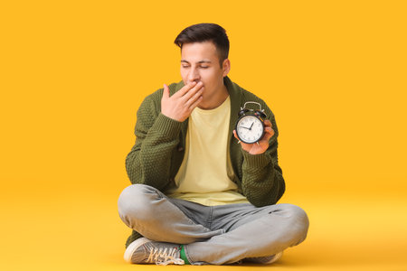 Tired man with alarm clock on color background. Concept of sleep deprivationの写真素材