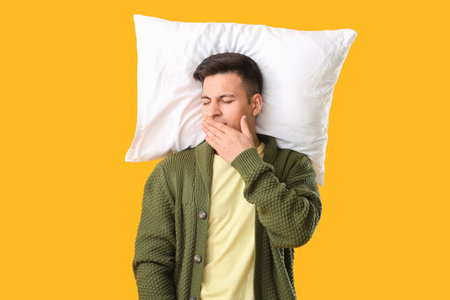 Tired man with pillow on color background. Concept of sleep deprivationの写真素材