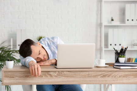Young man falling asleep during work in office. Concept of sleep deprivationの写真素材