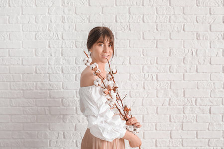 Beautiful young woman with cotton flowers on white brick backgroundの写真素材