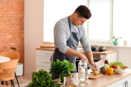 Young man with recipe book preparing fresh lemonade in the kitchenの写真素材