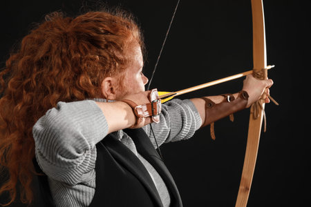 Beautiful female archer with bow on dark background