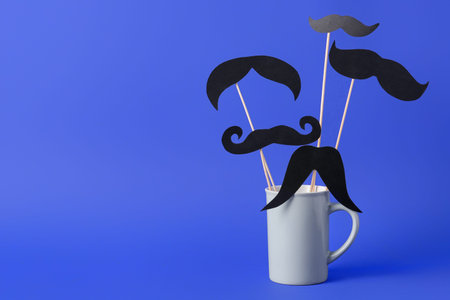 Wooden sticks with different paper mustaches in cup against blue backgroundの写真素材
