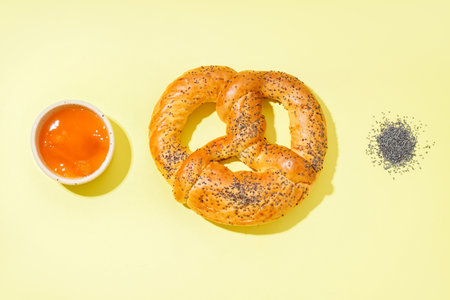 Tasty pretzel, jam and poppy seeds on yellow backgroundの写真素材