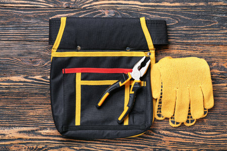 Pliers, tool belt and gloves on wooden background