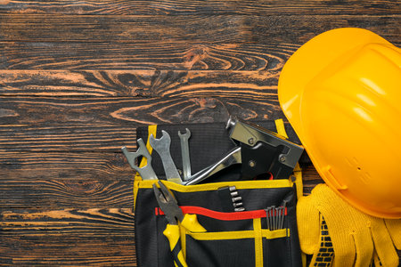 Pliers in tool belt, hardhat and gloves on wooden backgroundの写真素材