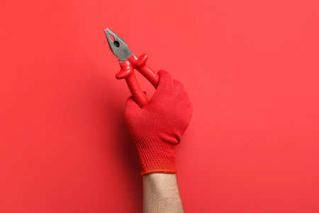 Male hand in gloves holding pliers on red backgroundの写真素材