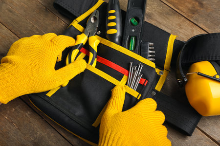 Male hands in gloves taking tools from belt on wooden tableの写真素材