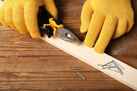Man with pliers pulling nail out from wooden plank on tableの写真素材