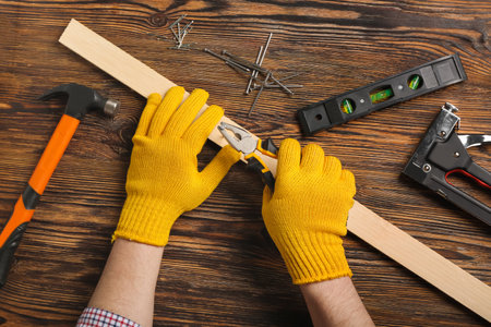 Man with pliers pulling out nail from wooden plank on tableの写真素材