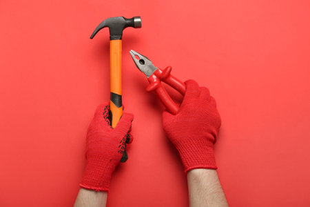 Male hands in gloves holding pliers and hammer on red backgroundの写真素材