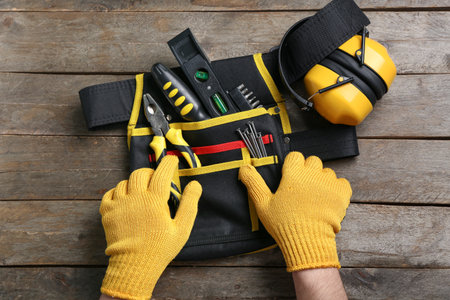 Male hands in gloves taking tools from belt on wooden tableの写真素材
