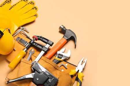 Pliers in belt with tools and gloves on beige background