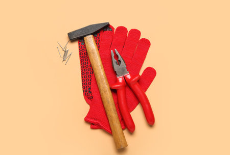 Pliers, hammer, nails and gloves on beige background