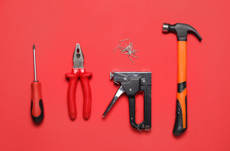Screwdriver, pliers, building stapler and hammer on red backgroundの写真素材