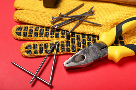 Pliers, nails, hammer and gloves on red background