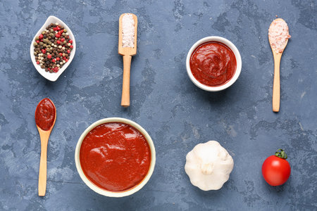 Composition with bowls of tomato paste, utensils and ingredients for sauce on blue grunge backgroundの写真素材