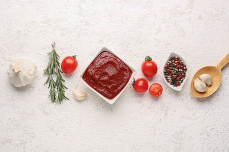 Composition with bowl of tasty tomato paste, garlic, peppercorn and rosemary on white grunge backgroundの写真素材