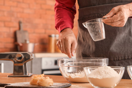 Man making dough for pasta at table in kitchen, closeup