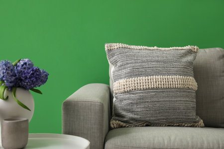Cozy gray sofa with soft cushion and vase of hyacinth flowers on table near green wallの写真素材