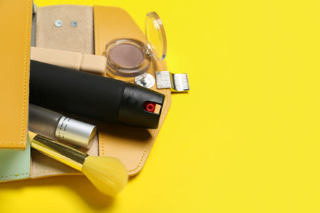 Bag with makeup products and pepper spray on yellow background, closeupの写真素材