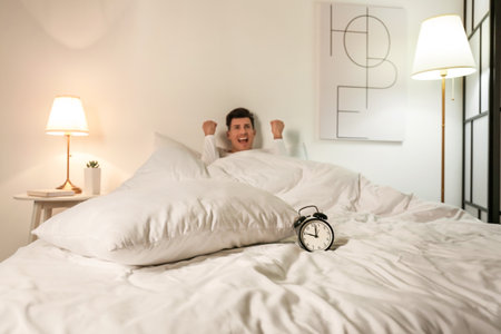 Stressed man with alarm clock suffering from insomnia in bedroomの写真素材