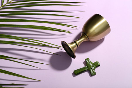 Cross made of palm leaves and wine cup on lilac background. good friday concept