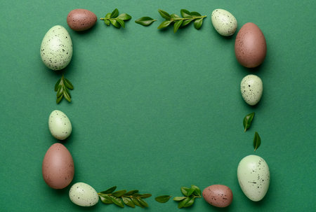 Frame made of Easter eggs and plant leaves on green backgroundの写真素材