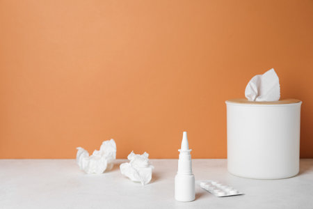 Nasal drops with pills and tissue box on table near orange wall. Allergy conceptの写真素材