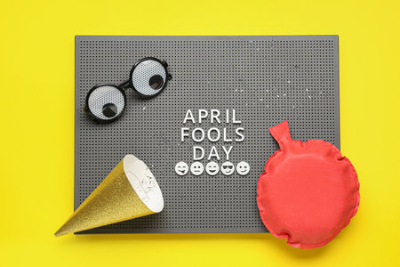 Board with text APRIL FOOLS DAY, funny decor and party hat on yellow backgroundの写真素材