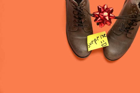 Paper with word SURPRISE, boots and bow on red background. April Fools' Day celebration