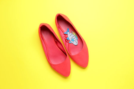 Female shoes with paper fish on yellow background. April Fools' Day celebration