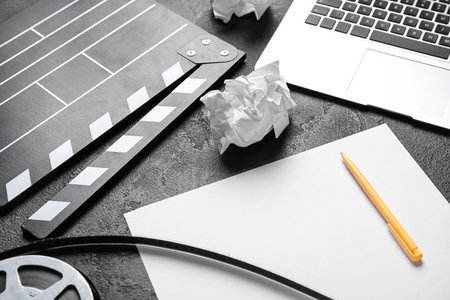 Blank paper sheet with movie clapper and film reel on dark background, closeup