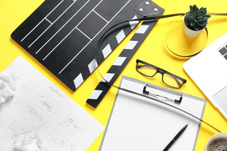 Clipboard with movie clapper, film reel and eyeglasses on yellow backgroundの写真素材