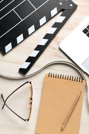 Notebook with film, movie clapper and laptop on light wooden backgroundの写真素材