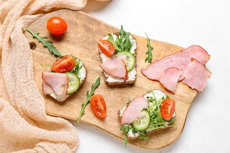 Wooden board of delicious sandwiches with cream cheese, ham and vegetables on light background, closeupの写真素材
