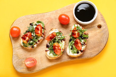 Wooden board of tasty sandwiches with cream cheese, arugula and tomatoes on color backgroundの写真素材