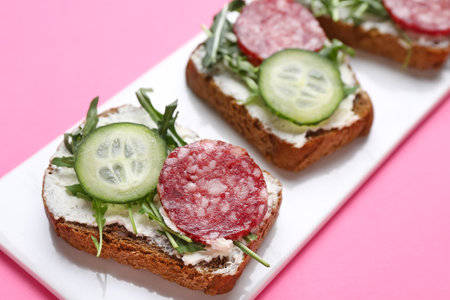 Plate of tasty sandwiches with cream cheese, salami, cucumber and arugula on color background, closeupの写真素材