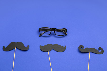 Wooden sticks with paper mustaches and eyeglasses on blue backgroundの写真素材