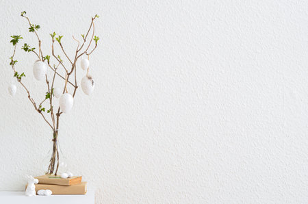 Vase with tree branches, Easter eggs and books on table near light wallの写真素材