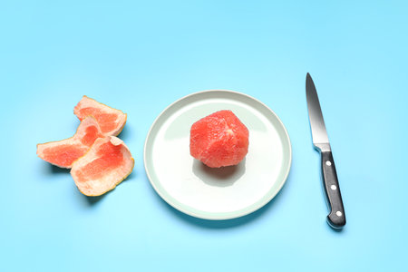 Plate with peeled grapefruit and knife on color backgroundの写真素材