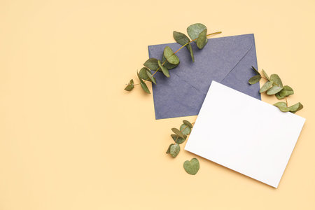 Composition with blank card, envelope and eucalyptus branches on color background